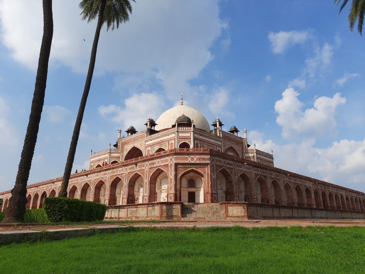 A dog on a lead walking past sandstone tombs in a Delhi park at dusk
